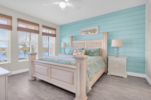 bedroom featuring light wood-type flooring, wood walls, ceiling fan, and baseboards