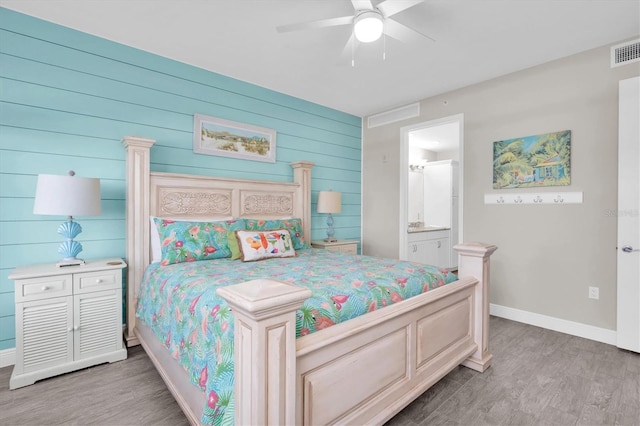 bedroom with ensuite bath, visible vents, baseboards, and wood finished floors