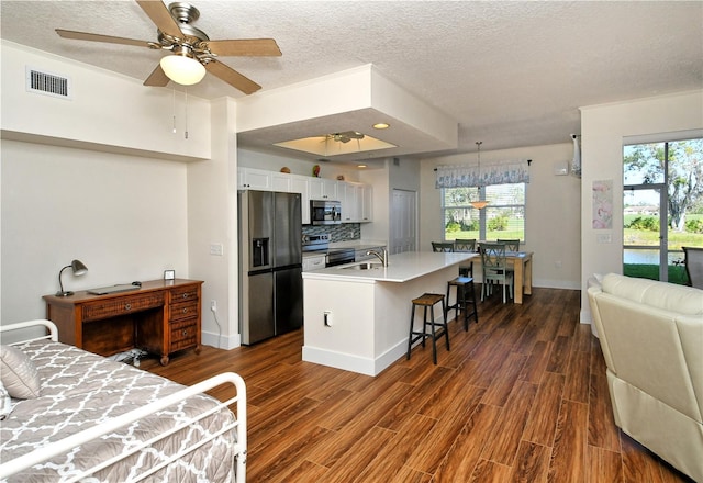 kitchen featuring a breakfast bar area, stainless steel appliances, visible vents, white cabinetry, and light countertops