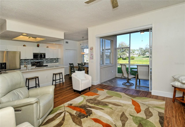 living area featuring dark wood-style floors, a textured ceiling, a ceiling fan, and baseboards