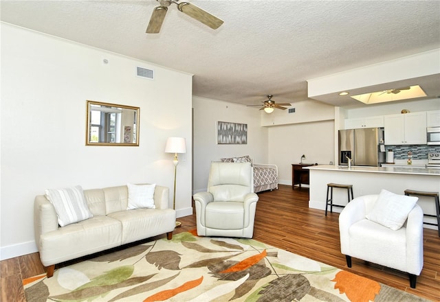 living area with a textured ceiling, wood finished floors, visible vents, baseboards, and a ceiling fan