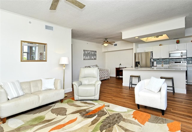 living room featuring dark wood finished floors, visible vents, a ceiling fan, a textured ceiling, and baseboards