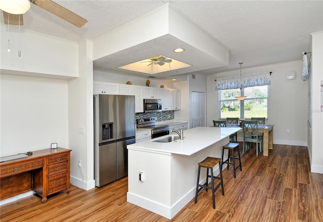 kitchen featuring pendant lighting, a center island with sink, stainless steel appliances, light countertops, and white cabinetry