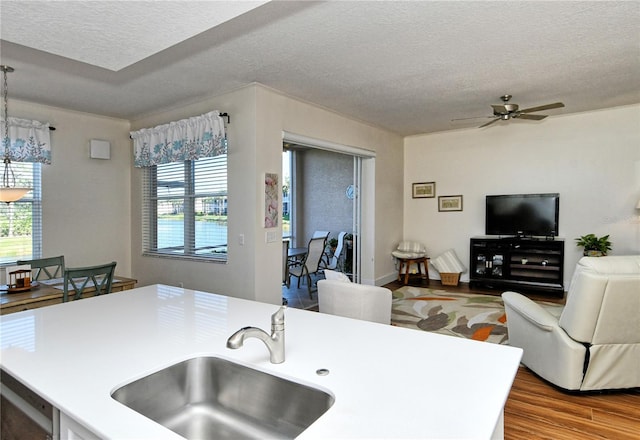 kitchen with light countertops, a ceiling fan, a sink, a textured ceiling, and wood finished floors