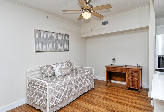 bedroom with ceiling fan, wood finished floors, visible vents, and baseboards