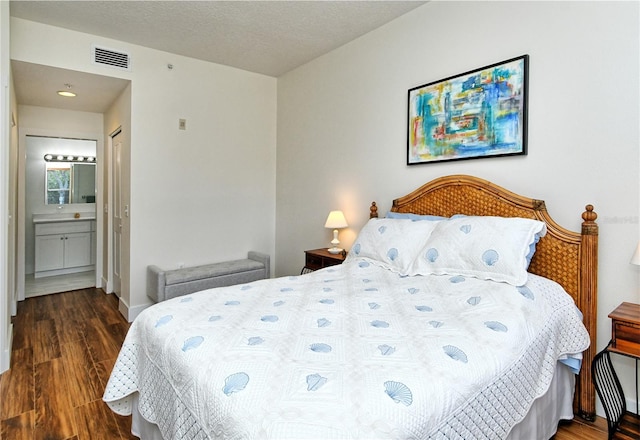 bedroom featuring visible vents, baseboards, dark wood-style floors, ensuite bath, and a textured ceiling