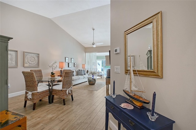 dining space with light wood-style flooring, a ceiling fan, baseboards, and high vaulted ceiling