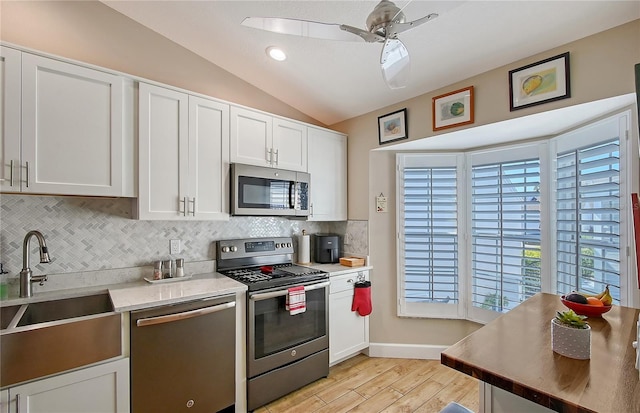 kitchen with light wood-style flooring, a sink, stainless steel appliances, vaulted ceiling, and backsplash