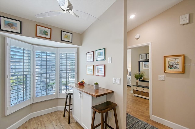 interior space with baseboards, ceiling fan, light wood-style floors, a kitchen bar, and butcher block counters