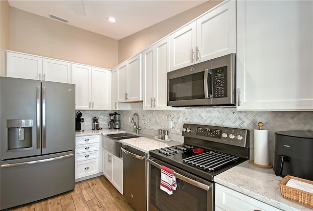 kitchen with a sink, decorative backsplash, white cabinetry, and stainless steel appliances