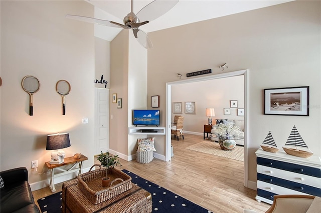 living area featuring a towering ceiling, baseboards, wood finished floors, and a ceiling fan