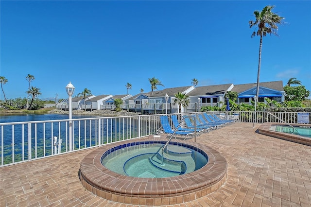 community pool with fence, a hot tub, a water view, a patio area, and a residential view