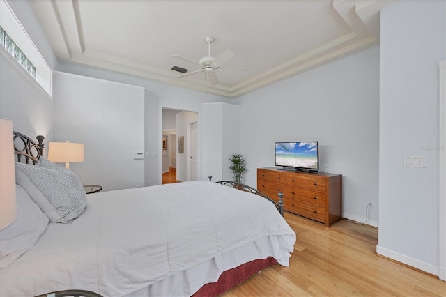 bedroom featuring a tray ceiling, baseboards, visible vents, and wood finished floors