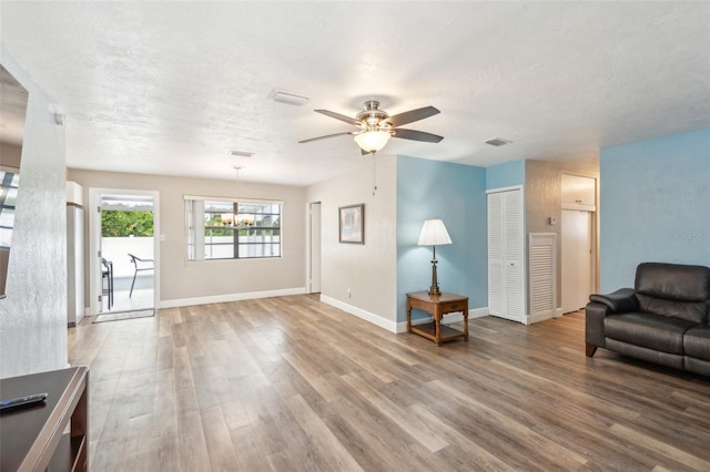 living room featuring ceiling fan with notable chandelier, wood-type flooring, and a textured ceiling