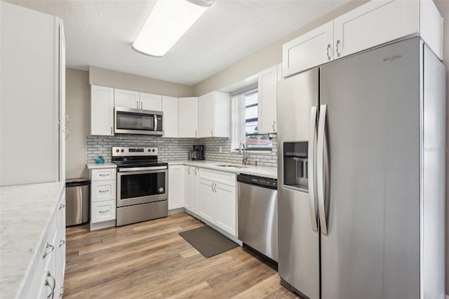 kitchen featuring appliances with stainless steel finishes, white cabinets, decorative backsplash, light hardwood / wood-style floors, and sink