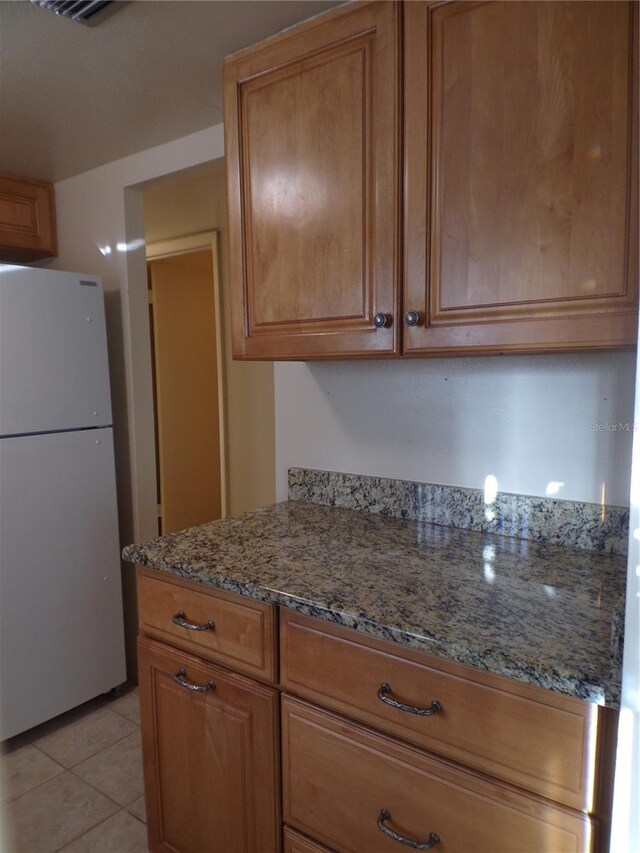 kitchen featuring stone counters, white fridge, and light tile patterned floors