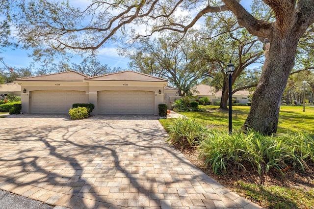 mediterranean / spanish-style home with a tiled roof, an attached garage, decorative driveway, a front lawn, and stucco siding