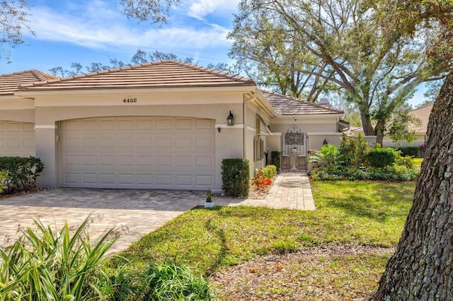 mediterranean / spanish-style home featuring a garage, a tile roof, decorative driveway, stucco siding, and a front lawn