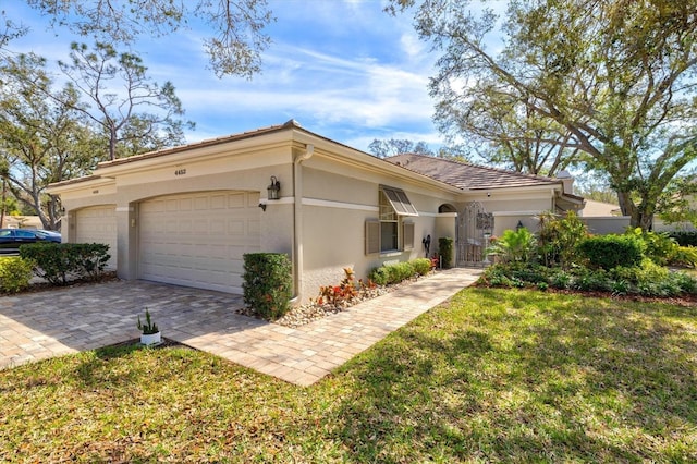 mediterranean / spanish home featuring a garage, decorative driveway, a front yard, and stucco siding