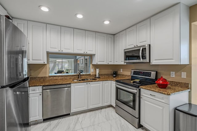 kitchen featuring appliances with stainless steel finishes, dark stone countertops, white cabinetry, a sink, and recessed lighting