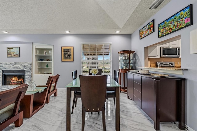 dining space featuring marble finish floor, recessed lighting, visible vents, a stone fireplace, and a textured ceiling