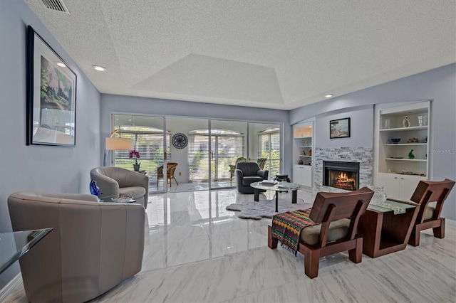 living room featuring a warm lit fireplace, visible vents, built in features, a raised ceiling, and a textured ceiling