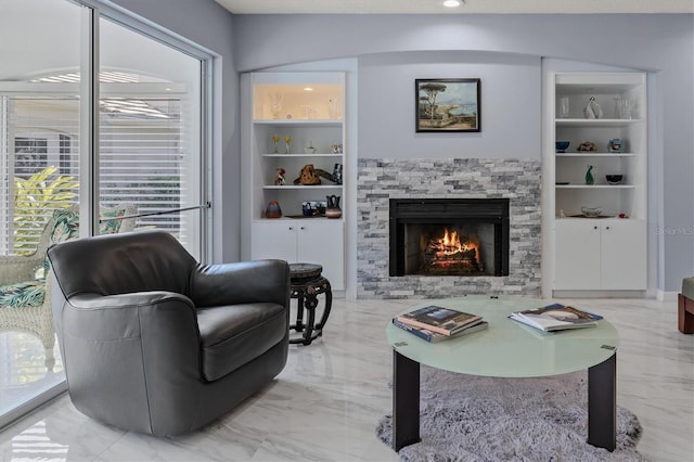 living area with marble finish floor, built in features, a wealth of natural light, and a stone fireplace