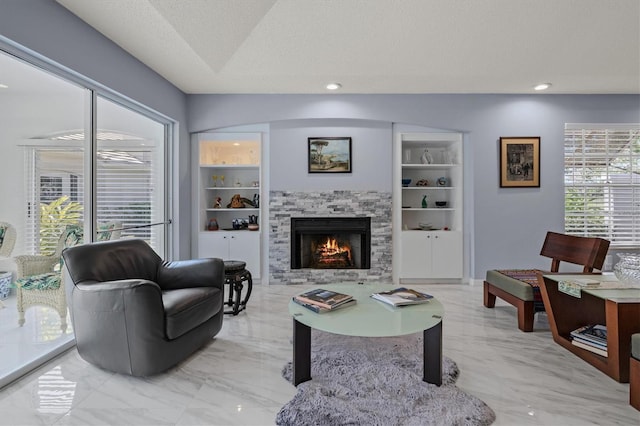 living room featuring built in shelves, marble finish floor, recessed lighting, a stone fireplace, and a textured ceiling