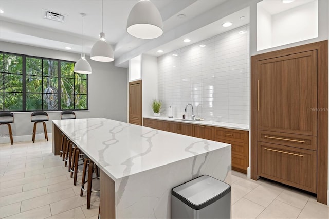 kitchen featuring a kitchen island, brown cabinets, a sink, and decorative light fixtures