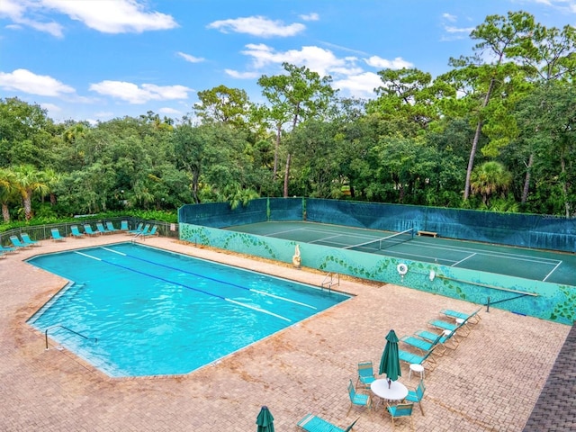 view of swimming pool with a tennis court and fence