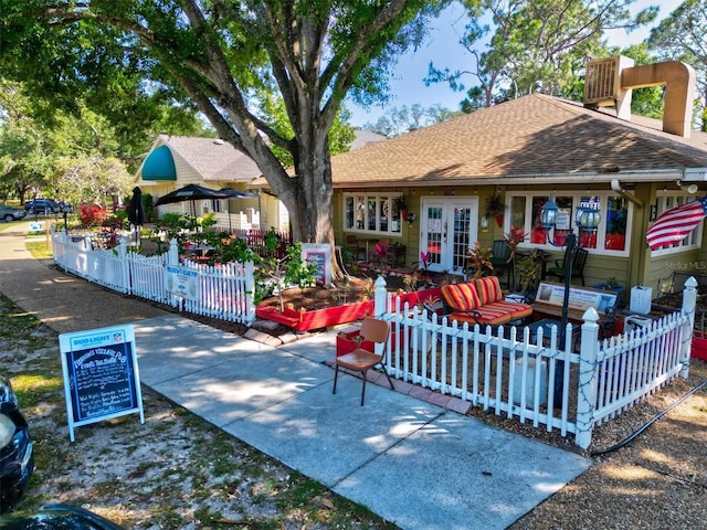 exterior space with french doors, a fenced front yard, and a shingled roof