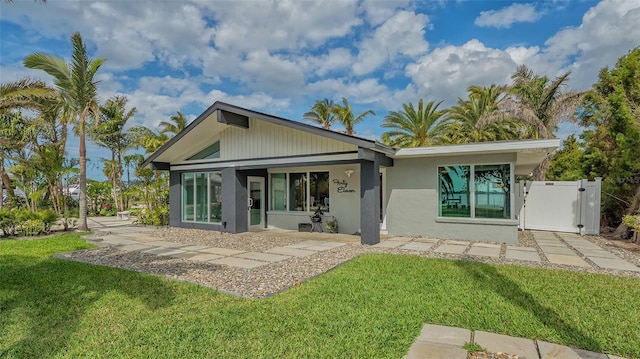 rear view of house featuring a lawn, a gate, and stucco siding