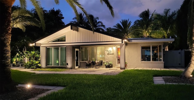 back of house with stucco siding and a yard