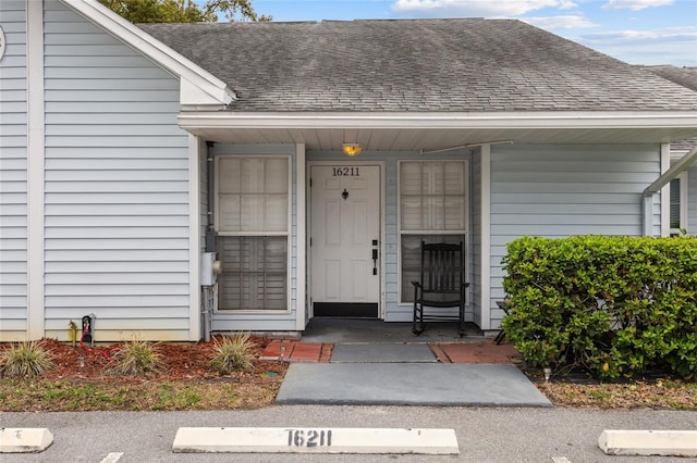 doorway to property with a shingled roof and a porch