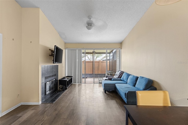 living area featuring a textured ceiling, a ceiling fan, baseboards, dark wood-style floors, and a tiled fireplace