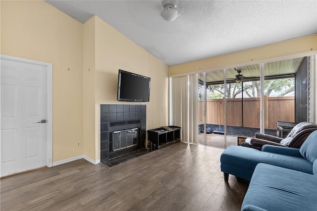 living room featuring a textured ceiling, wood finished floors, a ceiling fan, vaulted ceiling, and a tiled fireplace