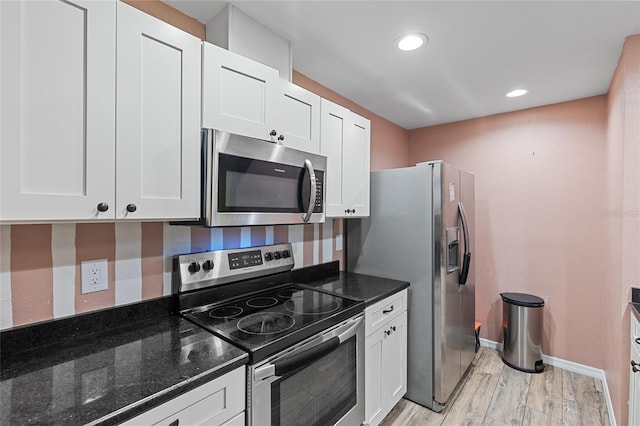 kitchen featuring appliances with stainless steel finishes, dark stone countertops, white cabinetry, and light wood-style floors