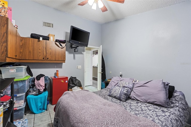 bedroom featuring light tile patterned floors, a ceiling fan, visible vents, and a textured ceiling