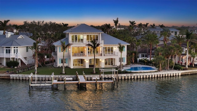 back house at dusk featuring a water view, a balcony, and a lawn