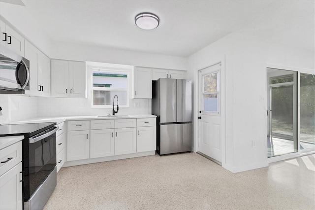 kitchen featuring stainless steel appliances, a sink, white cabinets, light countertops, and decorative backsplash