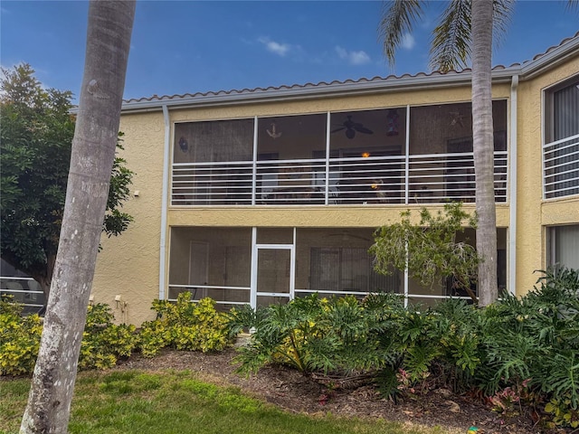 rear view of house featuring a sunroom, a tiled roof, and stucco siding