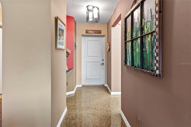 hall featuring a textured ceiling and baseboards