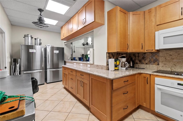 kitchen with white appliances, light stone counters, a paneled ceiling, backsplash, and light tile patterned flooring