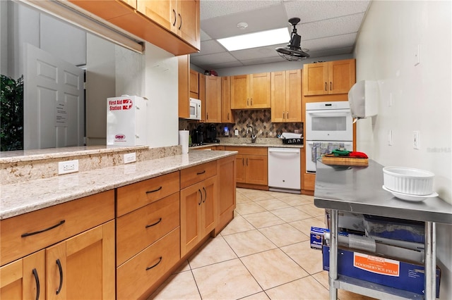 kitchen with white appliances, light tile patterned floors, decorative backsplash, light stone countertops, and a paneled ceiling