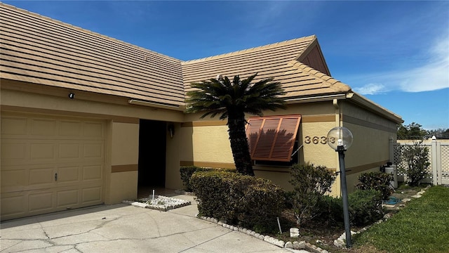 exterior space featuring a tiled roof, an attached garage, fence, and stucco siding