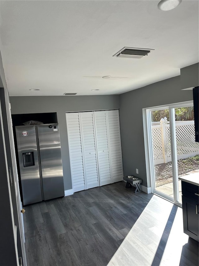 interior space with dark wood-style flooring, visible vents, baseboards, access to outside, and stainless steel fridge