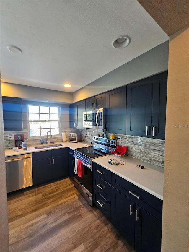 kitchen with a sink, light countertops, appliances with stainless steel finishes, tasteful backsplash, and dark wood finished floors