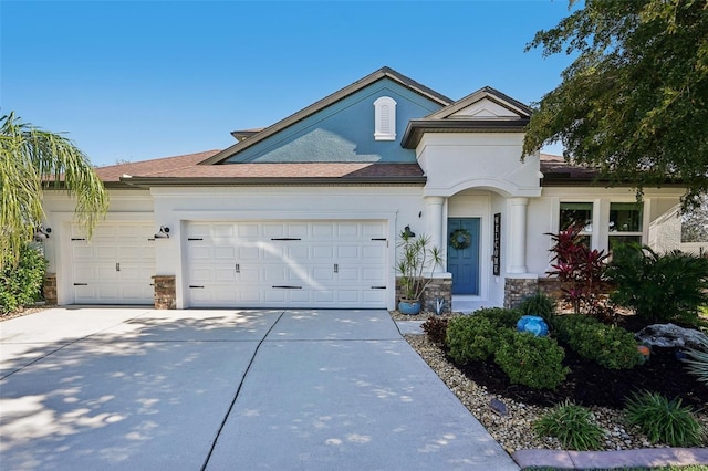 view of front facade with a garage, stone siding, driveway, and stucco siding