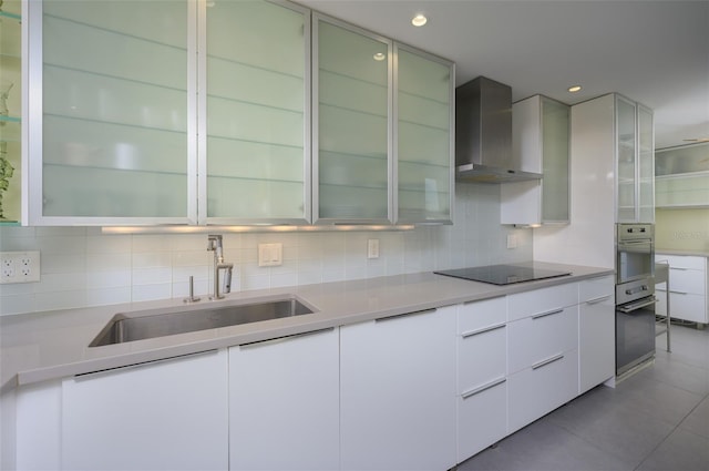 kitchen featuring wall oven, wall chimney exhaust hood, oven, black electric cooktop, and a sink