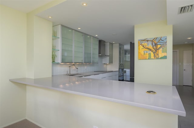 kitchen featuring visible vents, a sink, black electric stovetop, wall chimney range hood, and backsplash